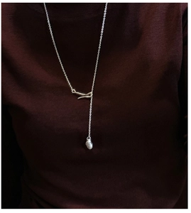 Detail of silver Y-shaped necklace with a baroque pearl pendant on dark red fabric