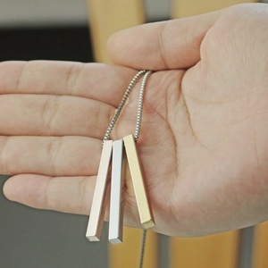 Detailed close-up of three cube pillar pendants in gold, silver, and rose gold finishes