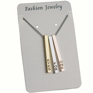 Detail view of gold silver and rose gold cubic bar pendants with engraved text on white card