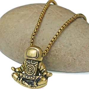 Macro detail of golden astronaut necklace pendant in meditation pose on pebble