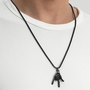 Close-up of black rock gesture hand pendant necklace worn over a white t-shirt