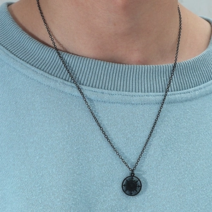 Détail d'un collier boussole noir mat porté sur un pull texturé bleu clair