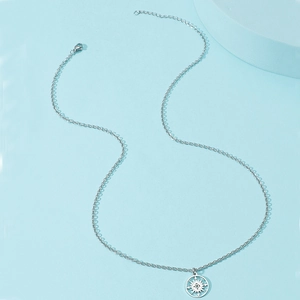 Collier boussole en acier inoxydable argenté sur fond bleu clair avec accessoires géométriques