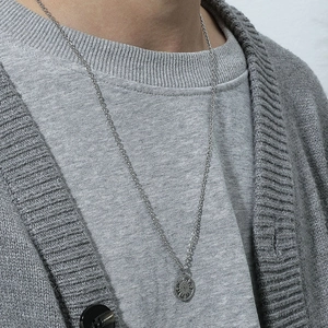 Détail du collier boussole argenté sur vêtement gris mettant l'accent sur le motif circulaire