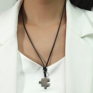 Détail d'un pendentif puzzle mat sur cordon noir porté sur un col de veste blanc