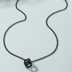 Detailed view of a black hollow cube pendant on a fine chain with artistic leaf shadows