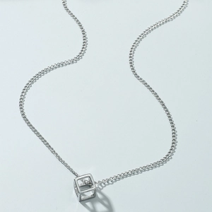 Macro shot of minimalist hollow cube pendant on silver cross chain with soft shadows