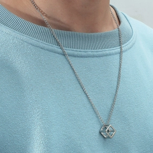 Detailed view of a silver hollow cube pendant on a thin metal chain worn over a blue hoodie