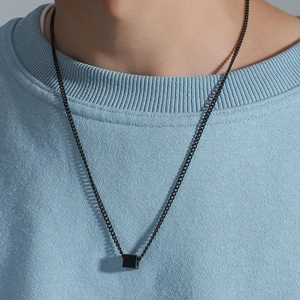 Close-up of a minimalist black geometric cube pendant on a fine chain worn by a male model