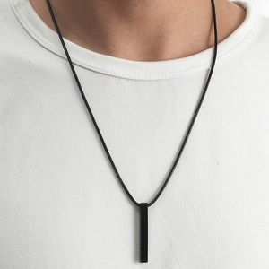 Gros plan d'un pendentif pilier rectangulaire noir sur un collier porté avec un t-shirt blanc