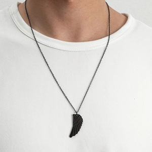 Gros plan d'un pendentif aile d'ange noir mat sur une chaîne porté sur un T-shirt blanc