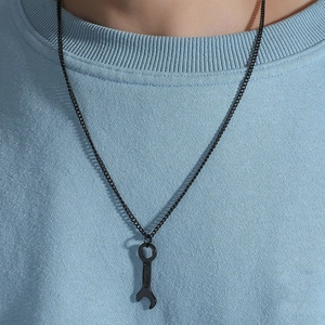 Close-up of black wrench pendant necklace on male model wearing blue streetwear