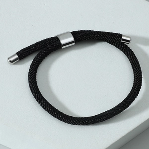 Gros plan d'un bracelet en cordon tressé noir avec fermoir coulissant argenté sur socle