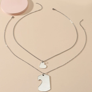 Polished stainless steel puzzle heart necklace set for couples on a beige background