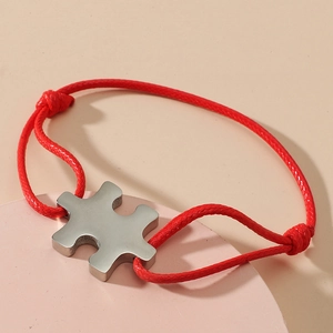 Detail of red braided bracelet with a polished silver puzzle piece metal charm