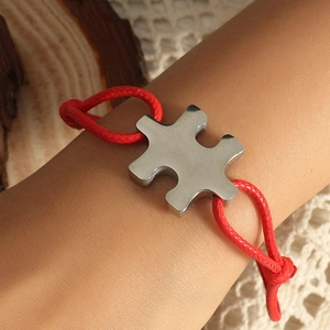 Handmade red cord puzzle bracelet featuring a polished stainless steel charm on wrist