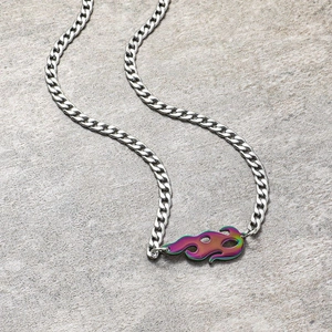 Détail macro d'une chaîne cubaine argentée avec pendentif flamme coloré sur fond de pierre