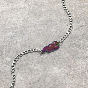 Gros plan sur la chaîne gourmette plate avec un pendentif flamme iridescent sur fond de pierre