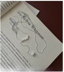 Detail of a minimalist silver chain necklace with a large pearl pendant on a book