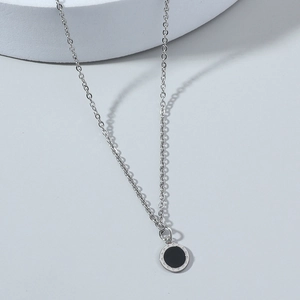 Minimalist silver chain necklace with a black round pendant on a smooth grey surface