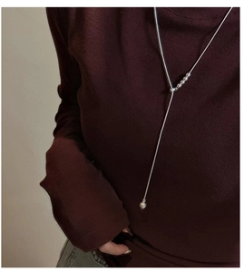 Detail of 925 silver Y-shaped long necklace with round beads on red knit background