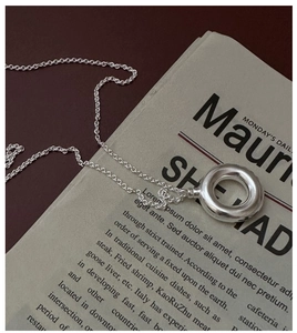 Detailed view of a silver hollow circle pendant necklace on a vintage newspaper background