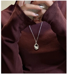 Gros plan du pendentif goutte d'argent poli sur un collier pull en tricot rouge