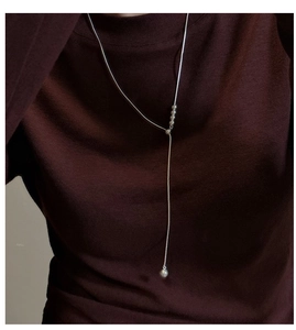 Detailed view of silver Y-shape snake chain necklace with beads on dark sweater