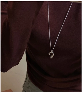 Macro view of minimalist S925 sterling silver water drop pendant on a long sweater chain