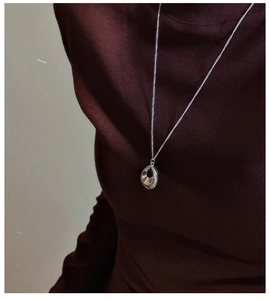 Détail d'un collier pendentif goutte d'argent sur un col roulé rouge foncé