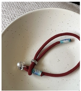 Detail of red braided rope bracelet with silver bell charm and blue silk thread accents