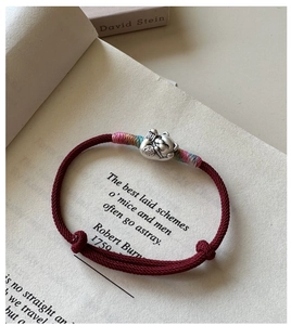 Gros plan du charm chat de fortune en argent S925 sur bracelet tressé rouge et livre