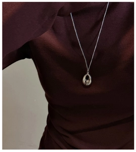 Détail du collier pendentif goutte d'argent poli porté sur un pull à col roulé foncé
