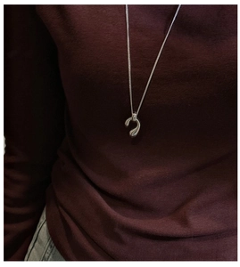 Macro detail of a sleek silver teardrop pendant necklace worn over a red knit sweater