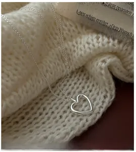 Detailed view of silver heart pendant necklace placed on a white knit sweater background