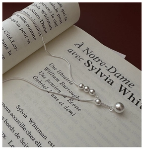 Close-up of minimalist 925 sterling silver sweater chain with bead pendant on vintage book