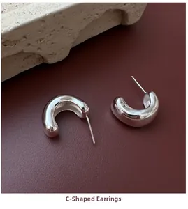 Detailed view of polished S925 sterling silver C-shaped earrings on textured backdrop