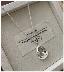 Vue macro d'un pendentif goutte en argent poli posé sur un coffret à bijoux gris