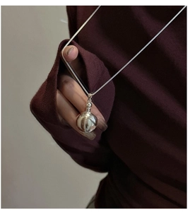 Polished silver sphere pendant on a fine chain styled over a dark red knit sweater