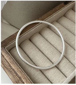 Macro shot of minimalist matte S925 sterling silver bangle resting on a wooden jewelry box