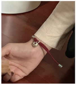 Close-up of red braided rope bracelet with silver Fu character lock charm on wrist