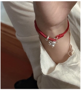 Close-up of a S925 sterling silver teapot charm on a red woven bracelet shown on a wrist