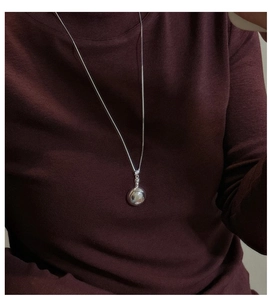 Close-up of polished S925 sterling silver round pendant necklace on a burgundy sweater