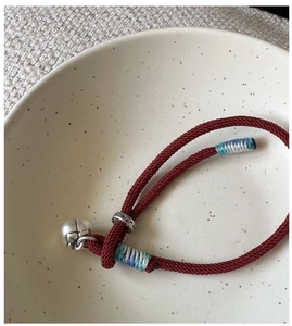 Detail of red braided cord bracelet with silver bell charm and blue thread wrap