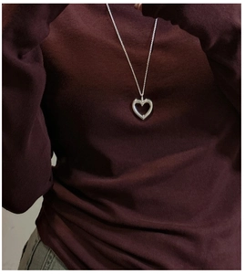 Close-up of matte silver hollow heart pendant necklace on a dark burgundy sweater