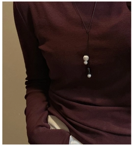 Detail of a minimalist long sweater necklace with white pearls and black teardrop pendant