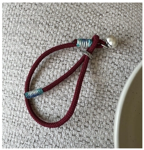 Detailed close-up of handmade red braided cord bracelet with silver bell and metal ring