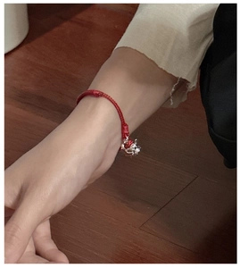 Detailed close-up of a red woven rope bracelet featuring a silver teapot charm on a wrist