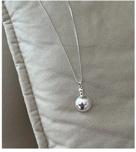 Macro shot of silver sphere pendant on a box chain over high-quality beige textured fabric
