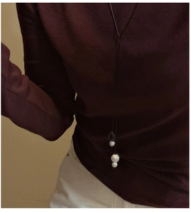 Detail of a minimalist long pendant necklace with pearl and bead on dark cord